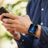 A man checks his phone while wearing a Fitaos health smartwatch